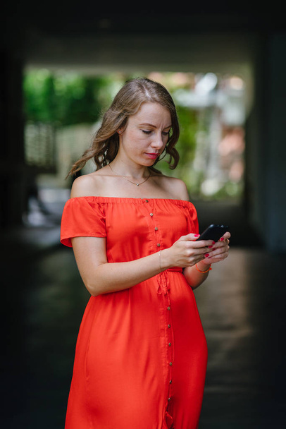 Portrait of a young, attractive Caucasian woman walking outdoor in park in the day. She was wearing a beautiful, light and comfortable orange dress and is smiling playfully. - Foto, Imagen