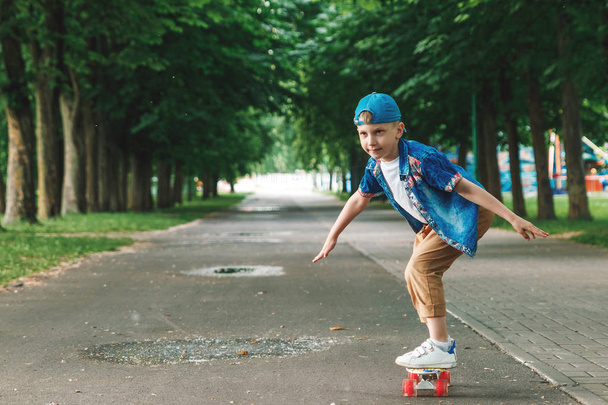 A small city boy and a skateboard. A young guy is riding in a park on a skateboard. City Style. City children. A child learns to ride a skateboard - Photo, image