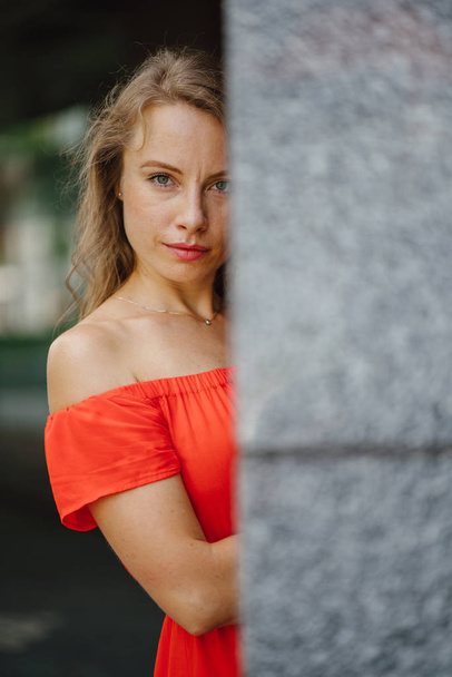 Portrait of a young, attractive European woman in an orange summer dress posing . She is blond with green eyes and is smiling confidently. - Valokuva, kuva