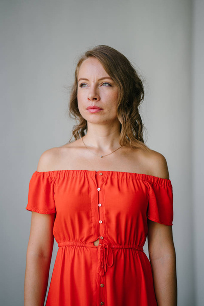 Portrait of a young, attractive European woman in an orange summer dress posing . She is blond with green eyes and is smiling confidently. - Fotó, kép