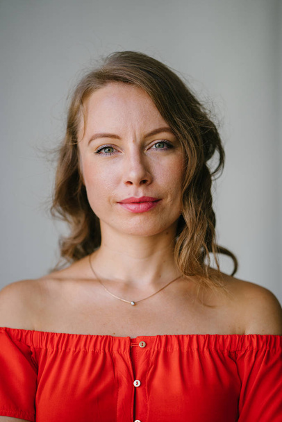 Portrait of a young, attractive European woman in an orange summer dress posing . She is blond with green eyes and is smiling confidently. - Фото, изображение