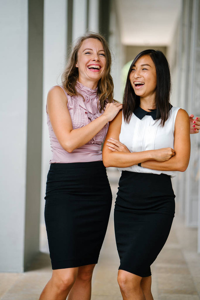 Portrait of a Chinese Asian woman and Caucasian white woman next to one another. They are both smiling  and are dressed professionally. - Фото, зображення