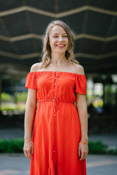 Portrait of a young, attractive Caucasian woman walking outdoor in park in the day. She was wearing a beautiful, light and comfortable orange dress and is smiling playfully. - Foto, Bild