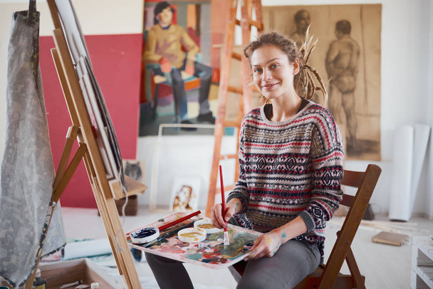 Artistic girl sitting in studio and paint on easel. - Foto, afbeelding
