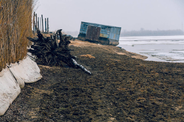 La cerca está hecha de ramas de sauce a lo largo de la orilla de un río congelado
 - Foto, Imagen
