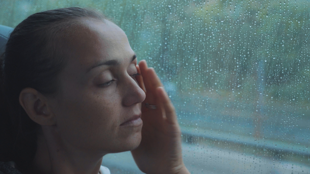 Portrét mladé smutné ženy při pohledu z okna mokré během cesty autobusem. - Záběry, video