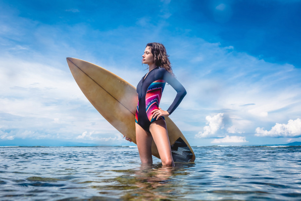 side view of attractive sportswoman in wetsuit with surfing board standing in ocean at Nusa dua Beach, Bali, Indonesia - Foto, imagen