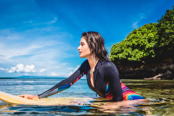 side view of pretty sportswoman in wetsuit on surfing board in ocean at Nusa dua Beach, Bali, Indonesia - Фото, изображение