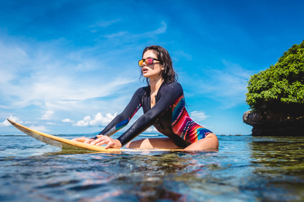 ウェット スーツとサングラス ヌサドゥア ビーチ、バリ、インドネシアの海でサーフィン ボードのスポーツウーマン - 写真・画像