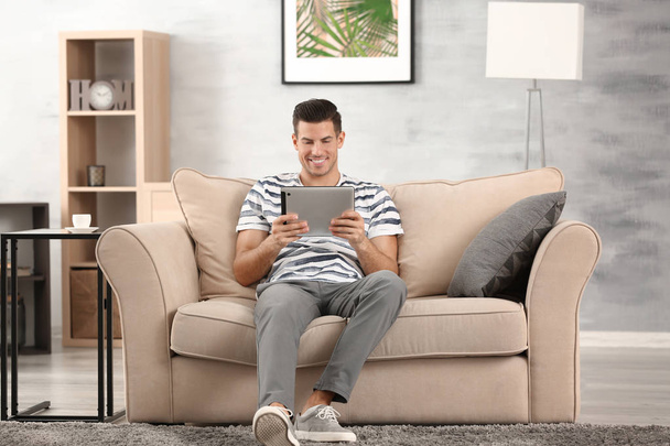 Handsome man using tablet pc while resting on sofa at home - Fotoğraf, Görsel