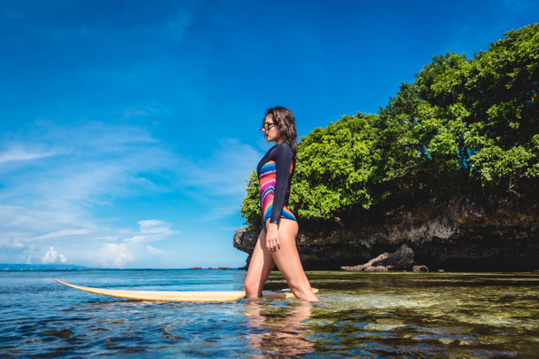 aantrekkelijke jonge vrouw in wetsuit met surfboard poseren in de Oceaan op Nusa dua Beach, Bali, Indonesië - Foto, afbeelding