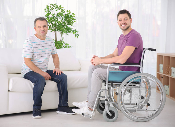 Зрелый мужчина и его сын в инвалидной коляске в помещении
 - Фото, изображение