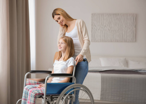 Young woman taking care of teenage girl in wheelchair indoors - Foto, immagini