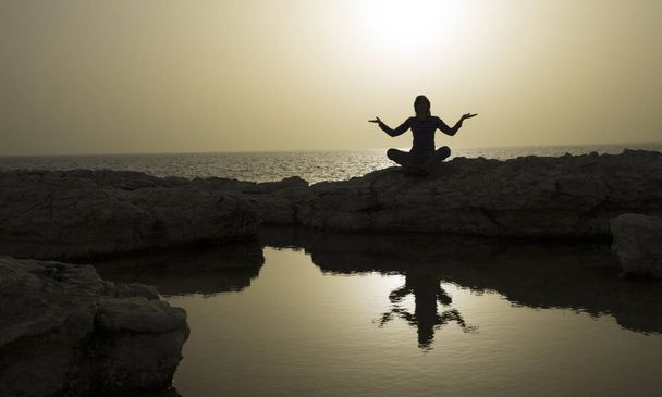 Frau in yogischer Pose am Meer. Die Silhouetten der Frau spiegeln sich in einem kleinen See. gleichmäßiges Licht ist wie Gold. - Foto, Bild