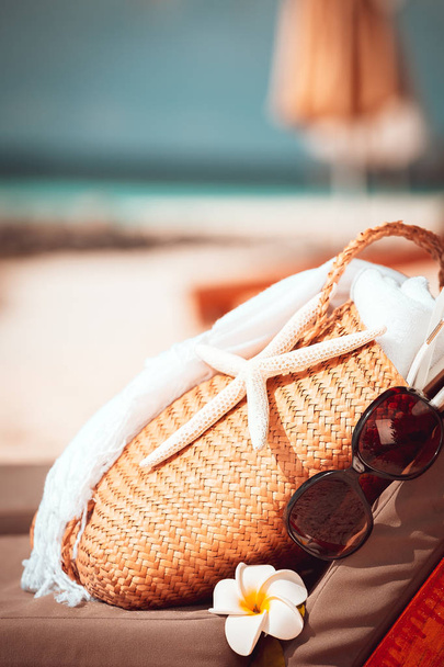 Пляжные флюиды, женская сумка и солнцезащитные очки на шезлонге украшены цветами франджипани и морской звездой, концепция летнего отдыха
 - Фото, изображение