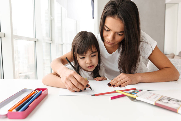 Image of beautiful people woman and child sitting at table in flat and drawing together picture with markers - Zdjęcie, obraz