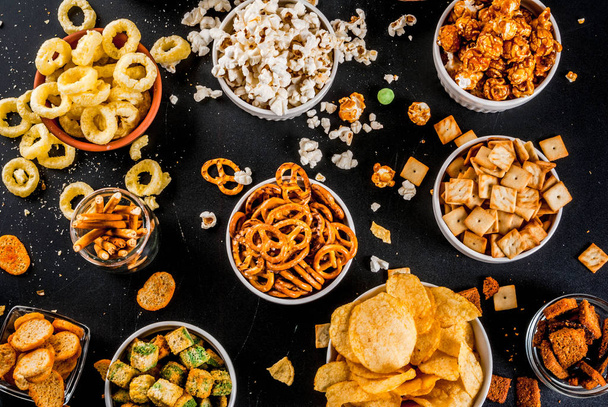 Variation different unhealthy snacks crackers, sweet salted popcorn, tortillas, nuts, straws, bretsels, back chalkboard copy space - Фото, изображение