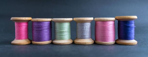 Set of pastel colors thread for sewing on a black background. Set of threads on bobbins retro style. Line coils with threads. Vintage accessories for sewing on the table. Multicolor spools of thread isolated - Photo, Image
