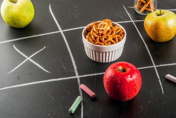 Tic tac toe healthy and unhealthy snack concept with crackers, chips and apples on black chalkboard - Photo, Image