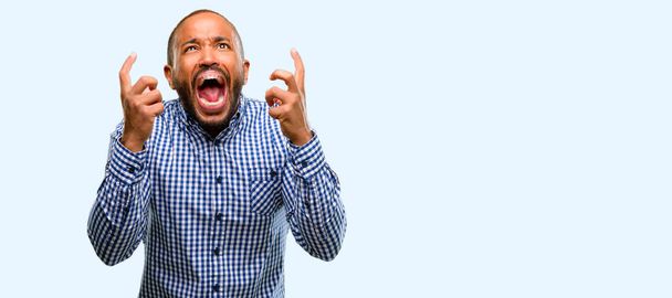 Uomo afroamericano con barba terrorizzato e nervoso che esprime ansia e gesto di panico, sopraffatto isolato su sfondo blu
 - Foto, immagini