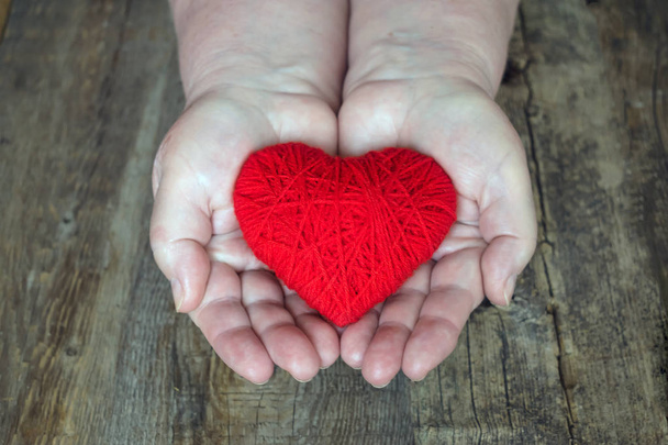 Organspende, hilf jemandem. Erwachsene Frauenhände geben rote Herzen. Hände einer erwachsenen Frau, Mutter hält ein rotes Herz in der Handfläche auf dunklem Holzgrund - Foto, Bild