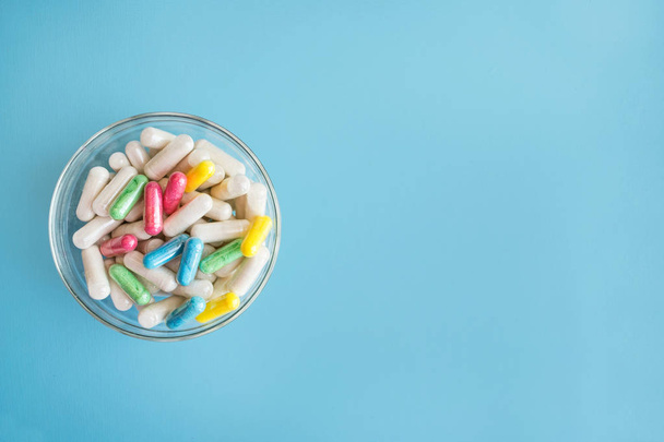 Colorful pills and medicines in glass plate on blue background. Different pills and another drugs capsules for illegal doping manipulations. Pharmacy antibiotic and antidepressant. - Foto, imagen