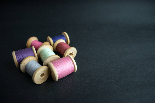 Set van pastel kleuren draad voor het naaien op een zwarte achtergrond. Het aantal threads op klossen retro stijl. Vintage accessoires voor naai op tafel. Multicolor spoelen van wol geïsoleerd - Foto, afbeelding