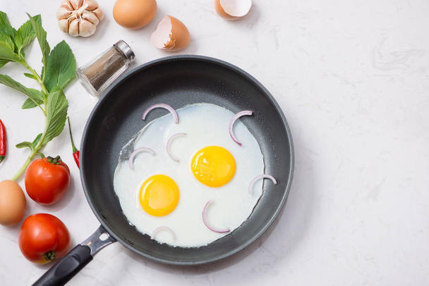 Eten in het proces, gebakken eieren in een koekenpan voor het ontbijt op een witte achtergrond. Daglicht. - Foto, afbeelding
