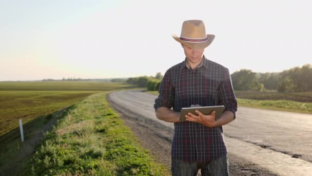 帽子の農民が道路に立っている間デジタル タブレットを使ってください。 - 映像、動画