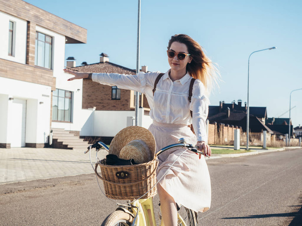 Menina bonita em chapéu e vestido de bicicleta de cruzador em subúrbio
. - Foto, Imagem