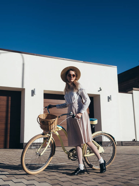 Pretty girl in hat and dress by cruiser bicycle in suburb. - Fotó, kép