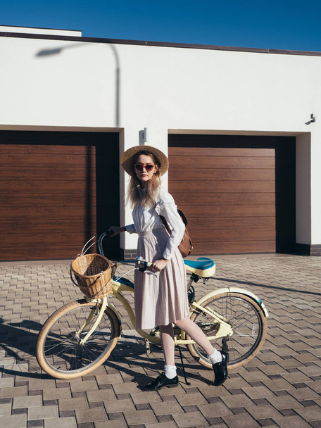 Pretty girl in hat and dress by cruiser bicycle in suburb. - 写真・画像