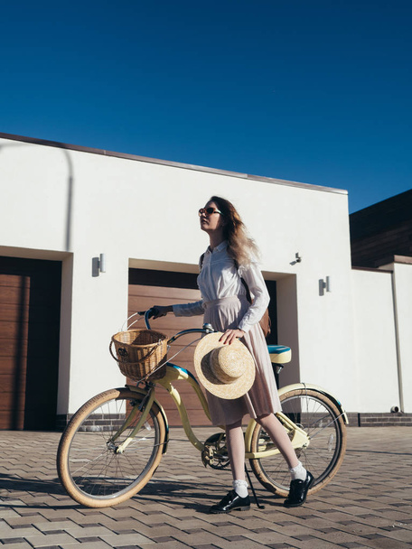 Pretty girl in hat and dress by cruiser bicycle in suburb. - Fotografie, Obrázek