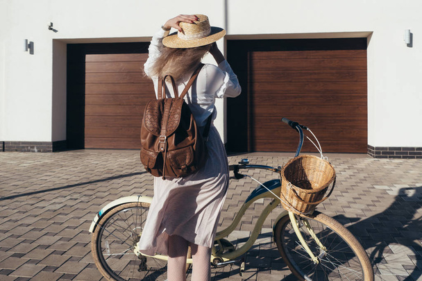 Ładna dziewczyna w kapelusz i sukienka przez cruiser rower w Przedmieście. - Zdjęcie, obraz