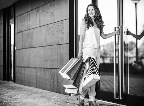 Happy young woman with shopping bags entering shop - Photo, image