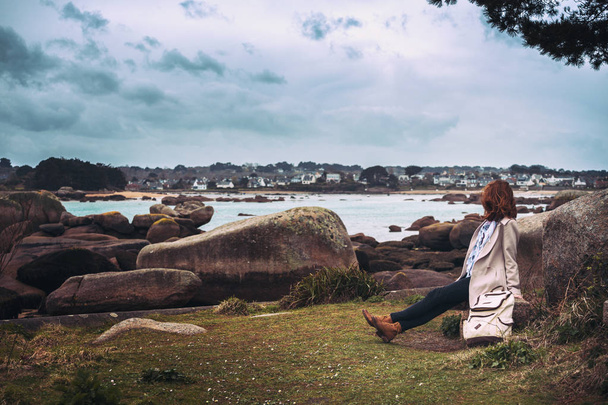 girl traveler sits on a bench near the sea and the shore at  the Tregastel, Brittany. Franc - Photo, Image