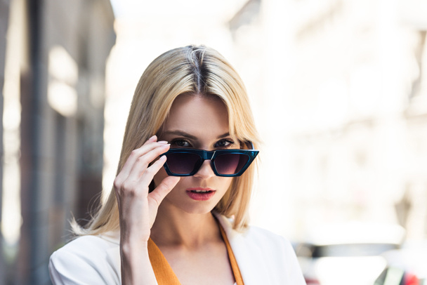 portrait of beautiful young blonde woman adjusting sunglasses and looking at camera - Foto, Imagem