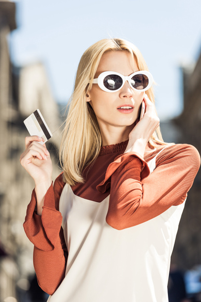 bella ragazza bionda in occhiali da sole in possesso di carta di credito e parlando con lo smartphone
 - Foto, immagini