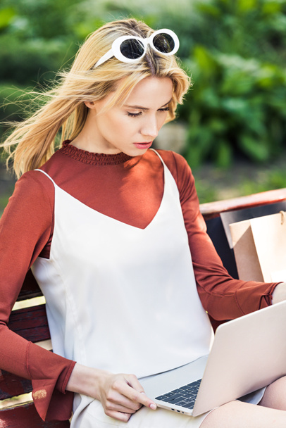 beautiful young blonde woman using laptop while sitting on bench - Photo, Image