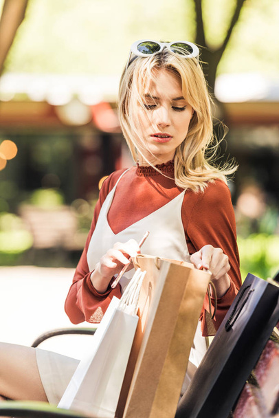 schöne junge Frau sitzt auf Bank und schaut in Einkaufstasche - Foto, Bild