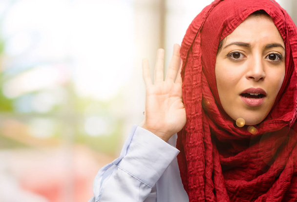 junge Araberin im Hijab, die die Hand am Ohr hält und versucht, interessante Nachrichten zu hören, die Kommunikationskonzept und Klatsch ausdrücken - Foto, Bild