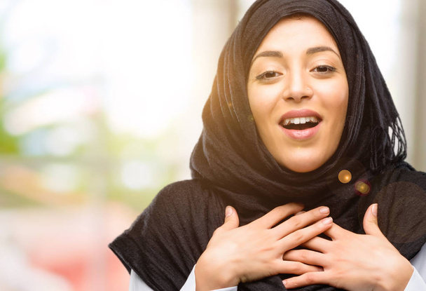 Молода арабська жінка в хіджабі має чарівну посмішку тримає руки на серці, бажаючи показати любов і співчуття
 - Фото, зображення