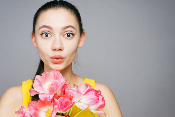 cute surprised young girl holding fragrant spring flowers and looking at the camera - Foto, Imagem