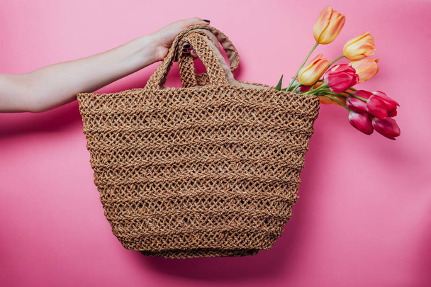 Studio shot of woman holding a straw bag with bouquet of tulips on pink background. Spring sale in stores. Accessories - Fotografie, Obrázek