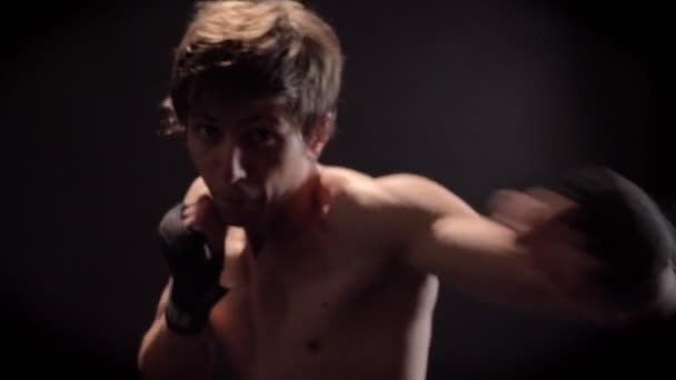 Young caucasian topless boxer boxing in front, looking at camera, jab, punch, black background 50 fps - Filmagem, Vídeo