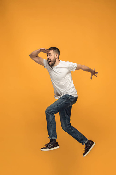 Freedom in moving. handsome young man jumping against orange background - Zdjęcie, obraz