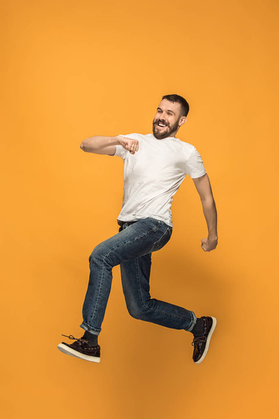 Freedom in moving. handsome young man jumping against orange background - Fotó, kép