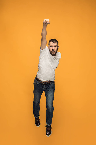 Freedom in moving. handsome young man jumping against orange background - Fotó, kép