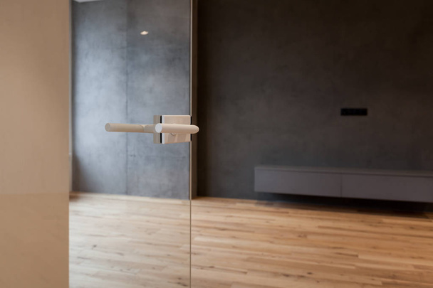 Porta de vidro com alça metálica aberta para a sala vazia com parede preta e piso de madeira
 - Foto, Imagem