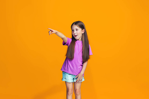 I choose you and order. The smiling teen girl pointing to camera, half length closeup portrait on orange studio background. The human emotions, facial expression concept. Front view. Trendy colors - Photo, image